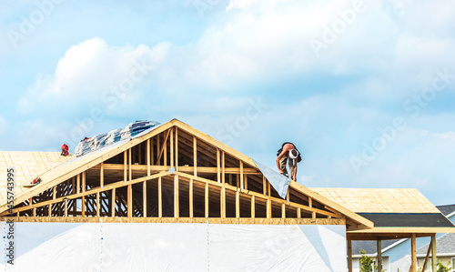 Bild auf Leinwand Worker installing on wooden roof of new house with couds blue sky
