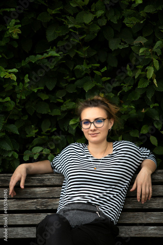 young brunette woman with glasses sitting on bench in park