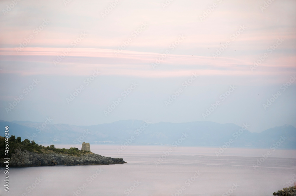 Promontory with an ancient watchtower at a strong afterglow of sunset over the bay of Marina di Camerota, Italy.