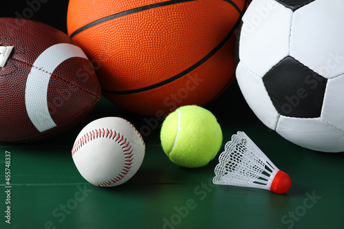 Set of different sport balls and shuttlecock on green wooden surface