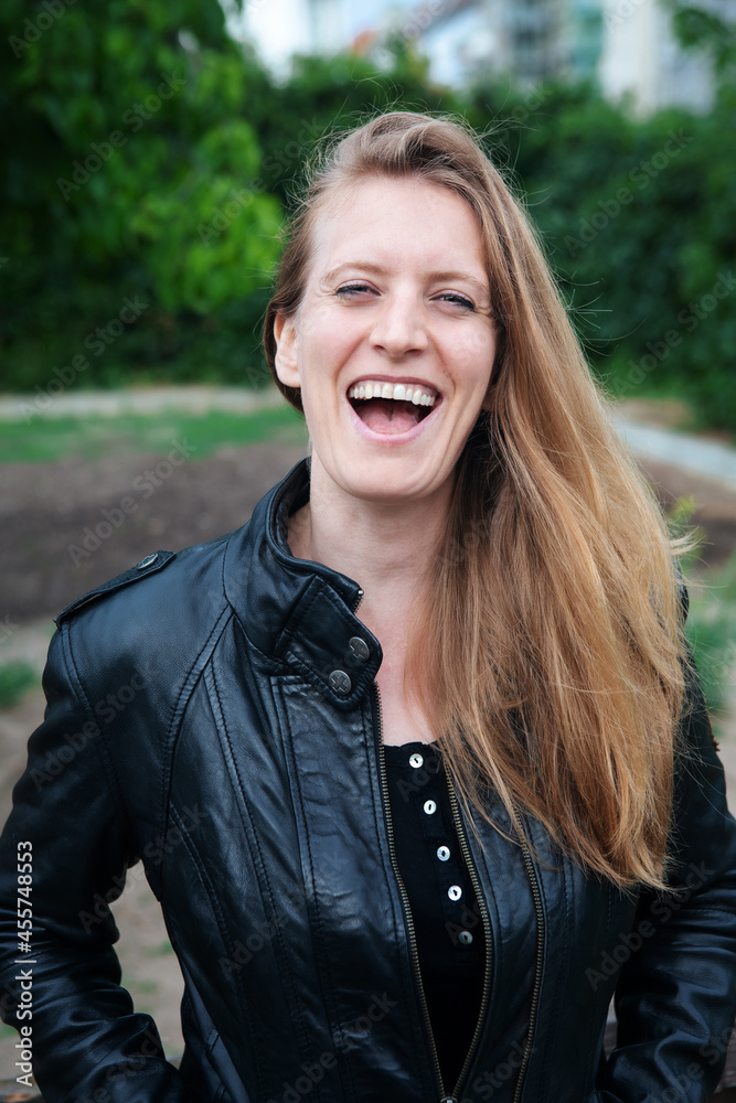 portrait of blond woman in black leather jacket standing outside and laughing