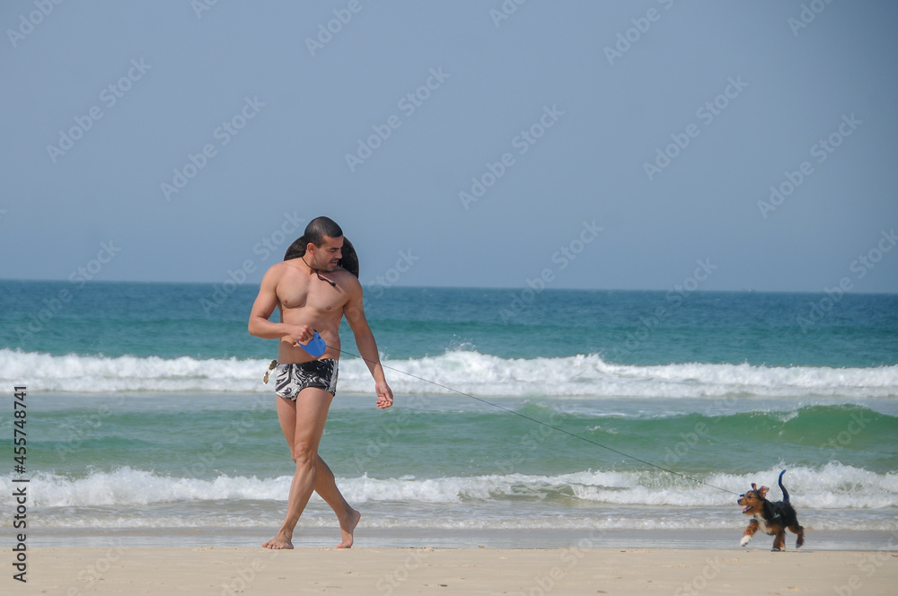 man gay walking in beach clothes, hat and sunglasses, on the sand with his little black dog, in the background the blue sea and its clear on a summer day
man gay walking in beach clothes, hat and sunglasses, on the sand with his little black dog, in the background the blue sea and its clear on a summer day
