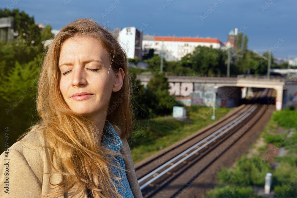 portrait of blond woman standing near railroad with her eyes closed