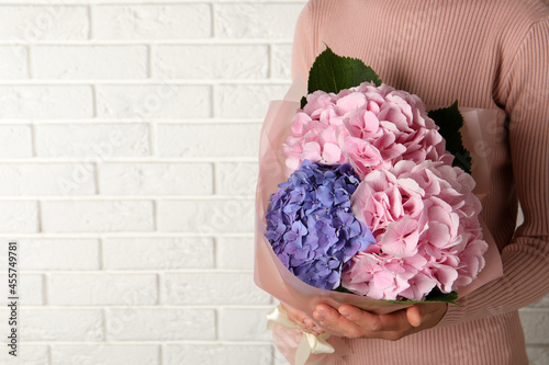 Woman with bouquet of beautiful hortensia flowers near white brick wall, closeup. Space for text