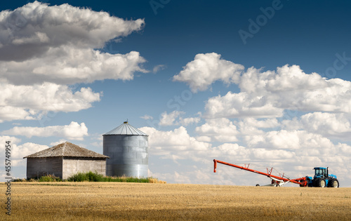 A farm tractor and auger filling a grain silo on a prairie wheat field in Rockyview County Alberta Canada. photo