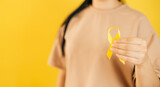 a woman holding a yellow gold ribbon in her hand on a yellow background, Bone cancer, awareness of childhood cancer, yellow September, the concept of World Suicide Prevention Day