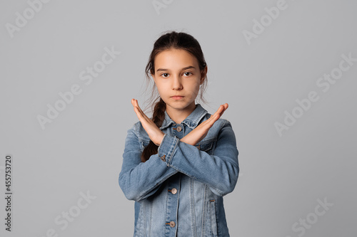 Obraz na plátně Serious young girl making X sign with her arms to stop doing something, standing over grey background, wearing in denim jacket