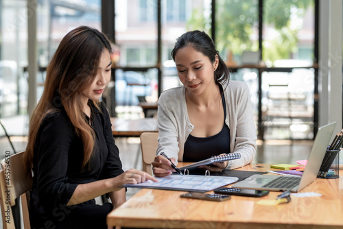 Team of young Asian businesswoman sitting at work brainstorming analyze holding a notebook pen pointing at the document the laptop is placed on the office desk.