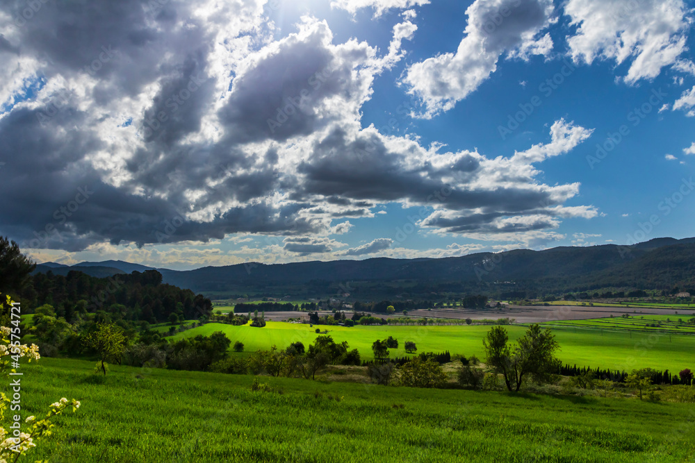 Green meadow in a day with white and gray clouds and sun rays.