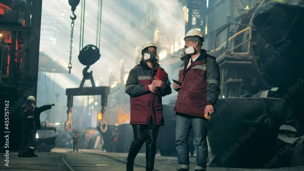 Steel mill colleagues in safety wear are walking along the factory Steel mill colleagues in safety wear are walking along the factory