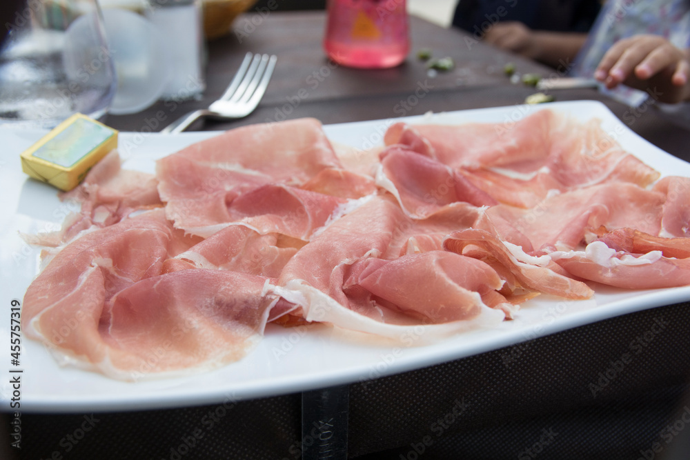 Prosciutto, an Italian dry-cured ham, thinly sliced and served uncooked in a white plate Prosciutto, an Italian dry-cured ham, thinly sliced and served uncooked in a white plate