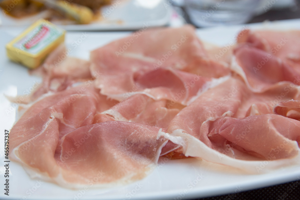 Prosciutto, an Italian dry-cured ham, thinly sliced and served uncooked in a white plate Prosciutto, an Italian dry-cured ham, thinly sliced and served uncooked in a white plate