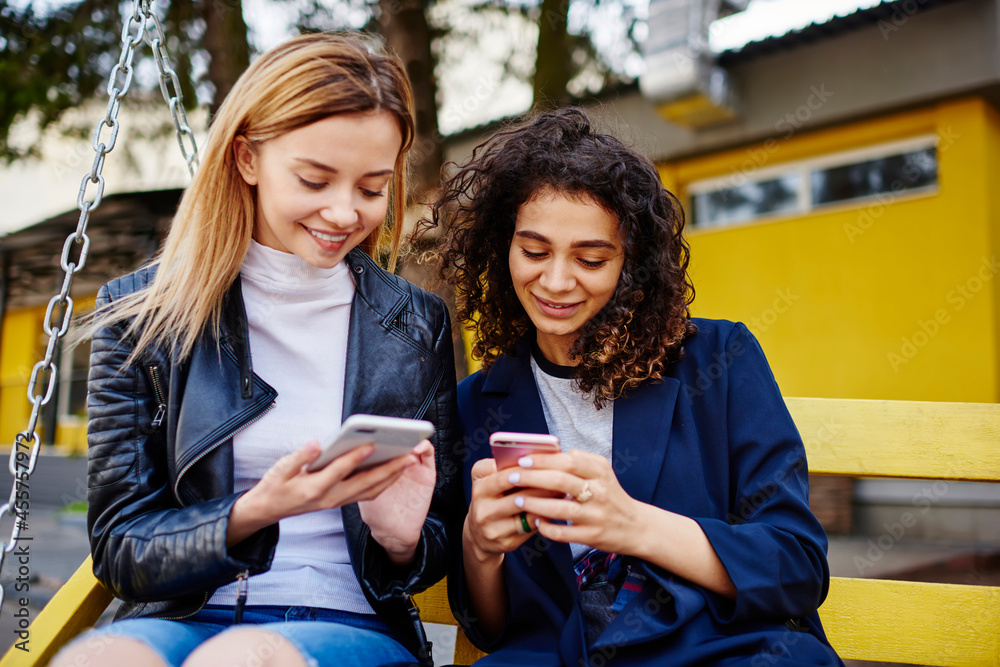 Multiracial women messaging on cellphones while sitting on bench