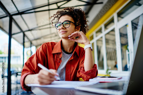 Dreamy woman doing homework in cafe