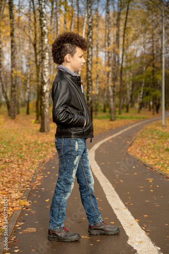 Curly brown-haired boy with a mohawk hairstyle in a leather jacket on an autumn background