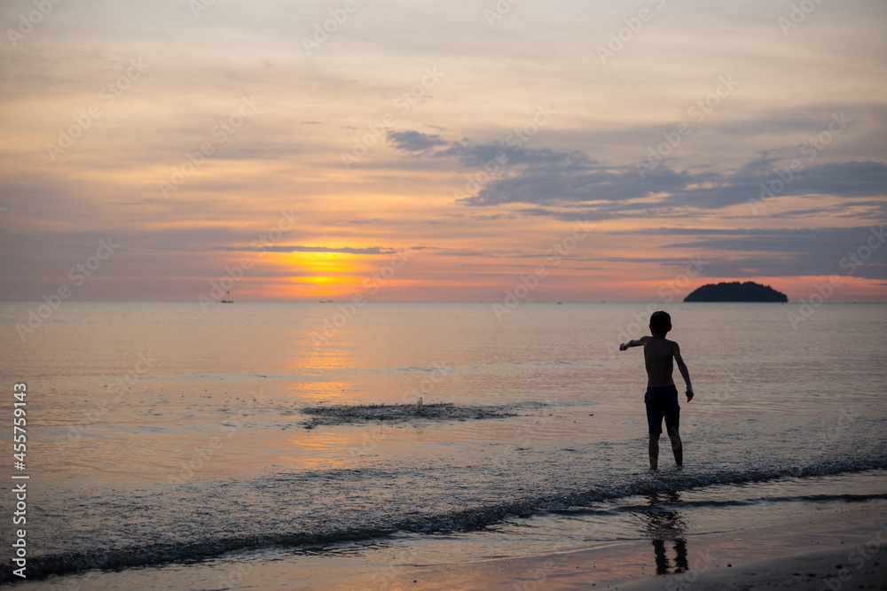 Boy throwing sand in rippling sea at sunset