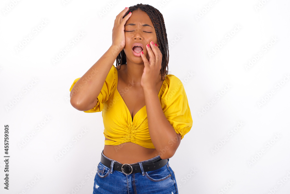 Young gloomy Young african american woman with braids over white wall , hiding face with hands pouting and crying, standing upset and depressed complaining about job problem. Young gloomy Young african american woman with braids over white wall , hiding face with hands pouting and crying, standing upset and depressed complaining about job problem.