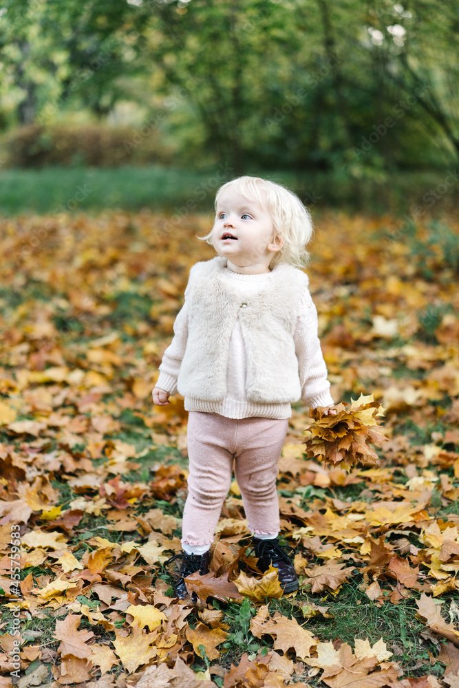 Happy little girl standing in autumn park with fallen leaves Happy little girl standing in autumn park with fallen leaves