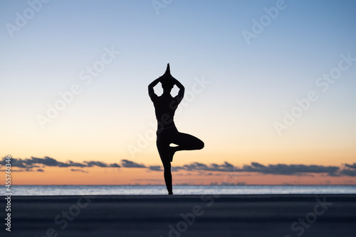 Unrecognizable female meditating in Vriksasana pose at sundown