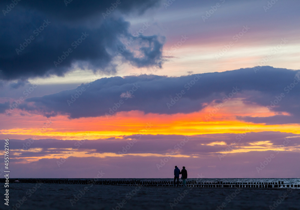 Paar geht nach dem Sonnenuntergang bei einem farbigen Gewitterhimmel am Strand der Ostsee spazieren 