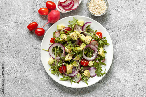 Fresh salad with arugula, tomatoes, avocado, red onion and radish, sesame