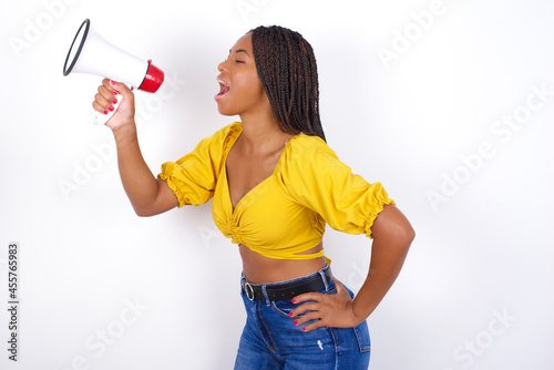 Funny Young african american woman with braids over white wall People sincere emotions lifestyle concept. Mock up copy space. Screaming in megaphone.