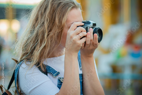 A young woman tourist in a denim sundress stands with cameras in an amusement park. © Вероника Преображенс