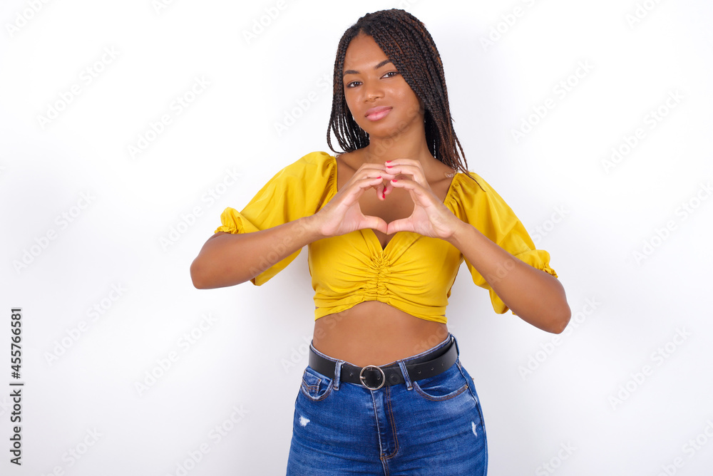 Serious Young african american woman with braids over white wall keeps hands crossed stands in thoughtful pose concentrated somewhere Serious Young african american woman with braids over white wall keeps hands crossed stands in thoughtful pose concentrated somewhere