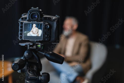 digital camera on tripod with businessman sitting in armchair on screen
