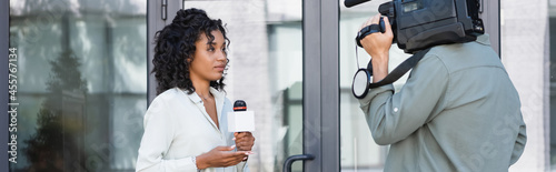 brunette african american journalist doing reportage near cameraman outside, banner photo