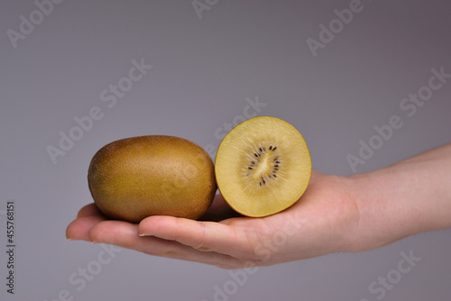 Hand holding gold kiwi isolated on grey background. Yellow kiwi fruit isolated. Gold kiwi fruit.