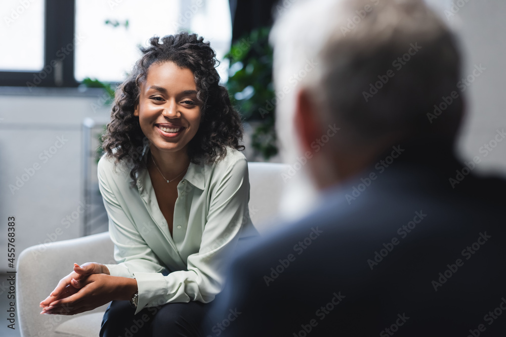 joyful african american journalist sitting in armchair and smiling near