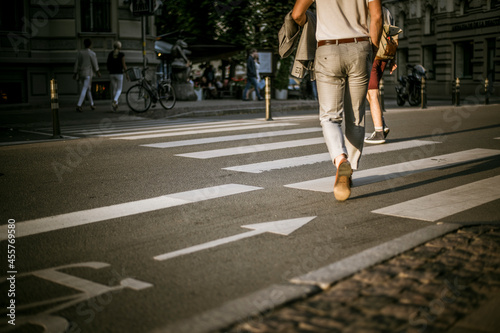 Pedestrian crossing at a sunset. Businessman in a suit is crossing a street. People crossing a street. © Jnis