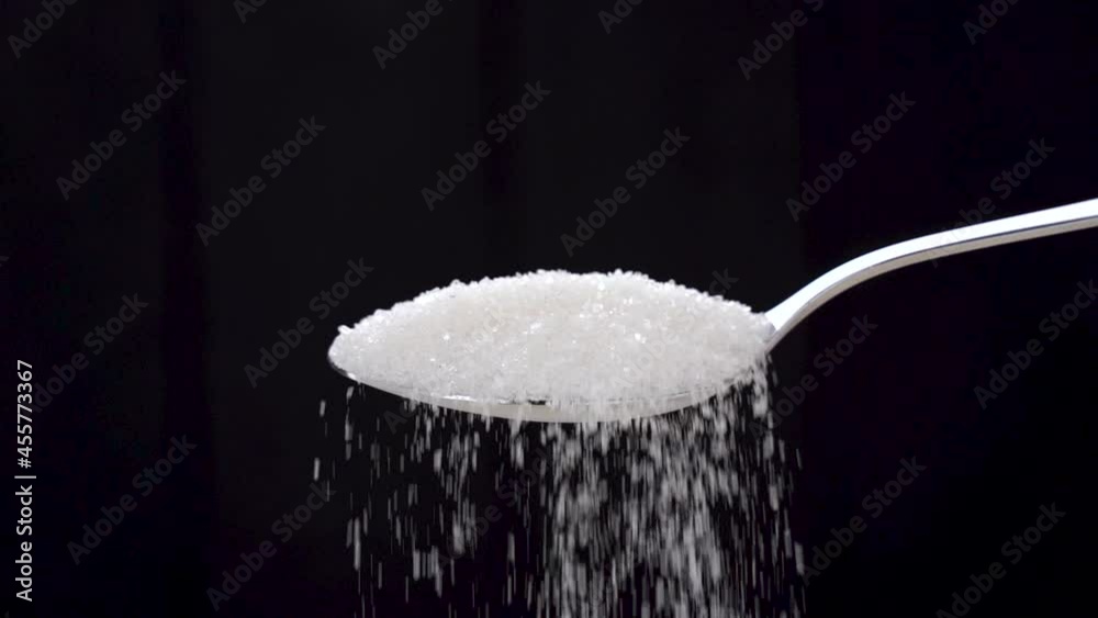 White sugar falls from a metal spoon on a black background. High quality FullHD footage