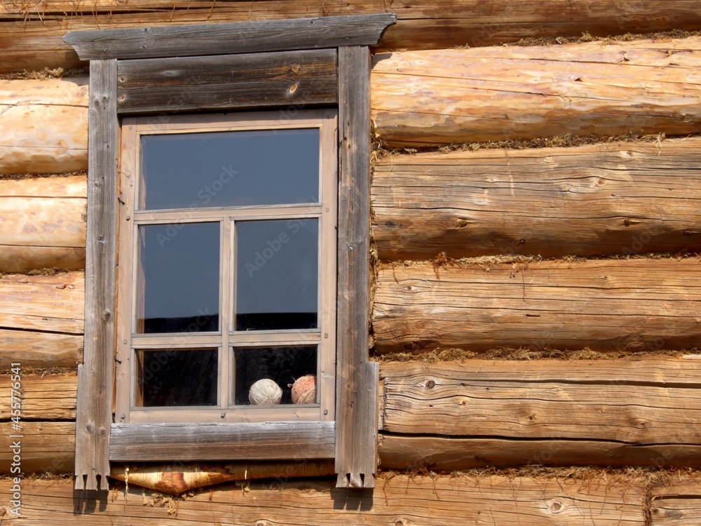 A window in an old wooden house with dark log wall. There are balls of yarn in the window of the old house. 