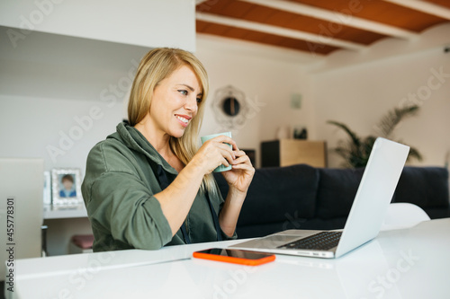 Middle age smiling blonde woman using a laptop in a livingroom