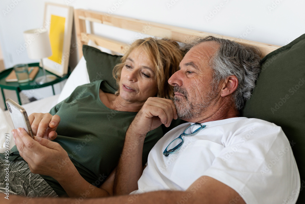Senior couple relaxing in bed with a mobile phone Senior couple relaxing in bed with a mobile phone