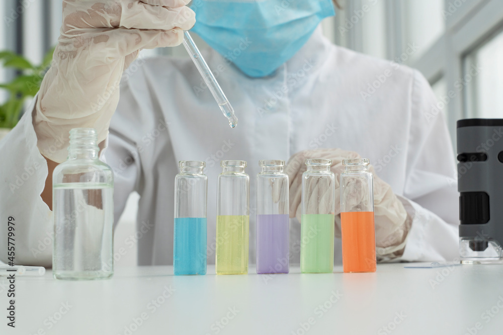 Close up image of five test tubes filled with liquids of different colors, boy's hand in protective glove is ready to put drop of solutioninto it, chemical experiments at home Close up image of five test tubes filled with liquids of different colors, boy's hand in protective glove is ready to put drop of solutioninto it, chemical experiments at home