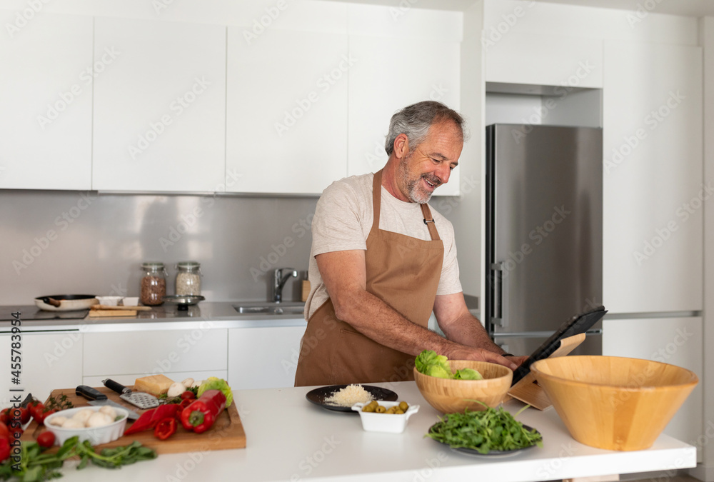 Joyful man cooking and using his tablet at kitchen
Joyful man cooking and using his tablet at kitchen