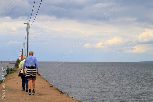 Senior man and woman walking next to the water. One cloudy summer day. The Swedish lake Vänern or Vanern. Lidköping, Sweden, Europe.