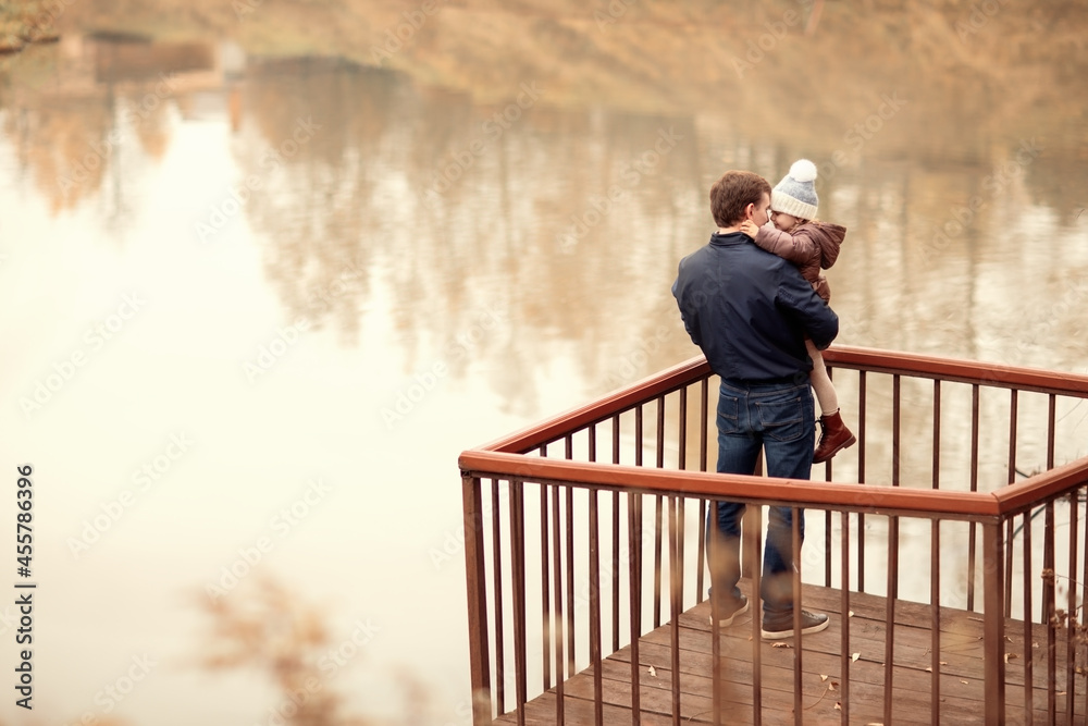 Fototapeta premium happy family walking in autumn park with lake,dad hugs and holds child, copy space, hello september