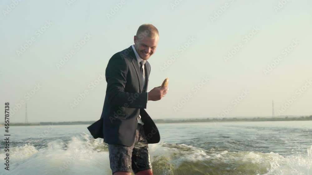 A surfer jumping on a wakeboard in a suit with a bun in his hands. The surfer eats a bun and rides a wakeboard. An experienced wakeboarder sprays water drops into the camera. A surfer jumping on a wakeboard in a suit with a bun in his hands. The surfer eats a bun and rides a wakeboard. An experienced wakeboarder sprays water drops into the camera.