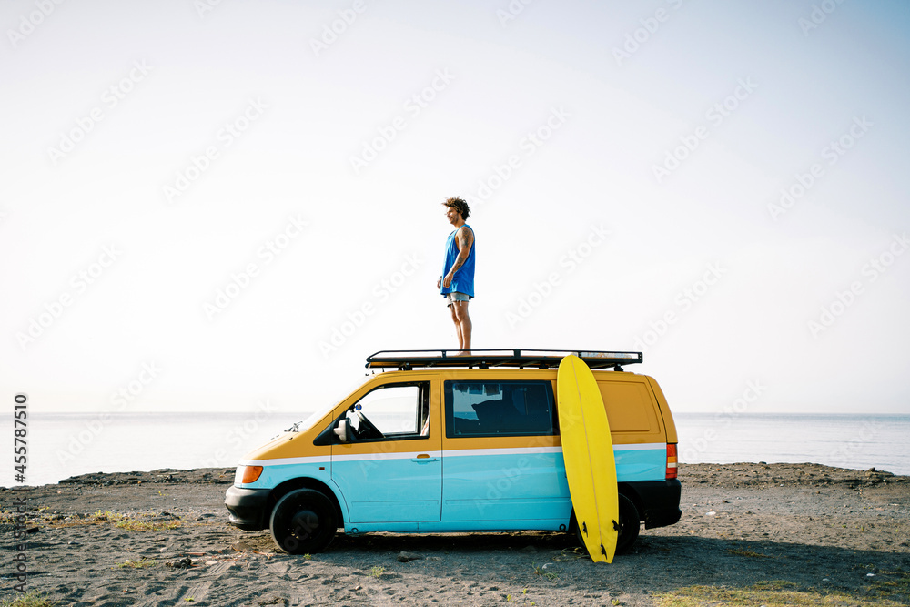 Travelling man with surfboard standing on van Travelling man with surfboard standing on van