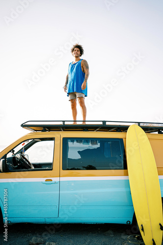 Travelling man with surfboard standing on van photo