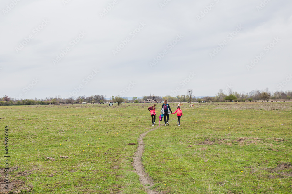 Family relax in nature reserve, mother with daughters walking in nature, spring landscape.