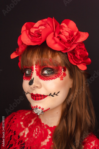 Portrait detail of the face of a beautiful happy girl with Day of the Dead makeup on black background.