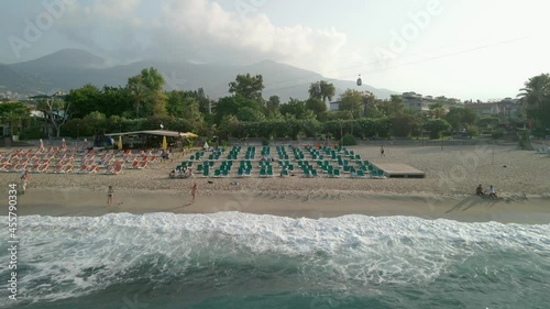 Beach, top view of waves crashing against the beach, with people and umbrellas on the shore on a beautiful summer day. Cleopatra Beach, Alanya