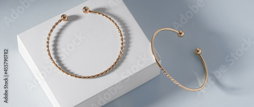 Panoramic shot of two modern golden bracelets on white box on blue background with copy space