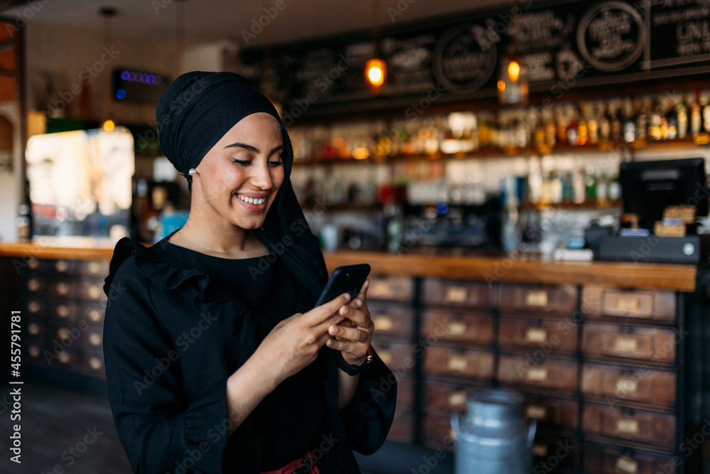Cheerful stylish Muslim woman using cellphone in cafe Cheerful stylish Muslim woman using cellphone in cafe