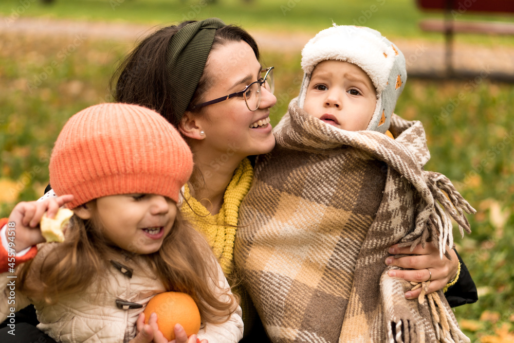 Obraz premium Young Woman Mom And Little Cute Preschool Minor Children In Orange Plaid At Yellow Fallen Leaves Nice Smiling Look At Camera In Cold Weather In Fall Park. Childhood, Family, Motherhood, Autumn Concept